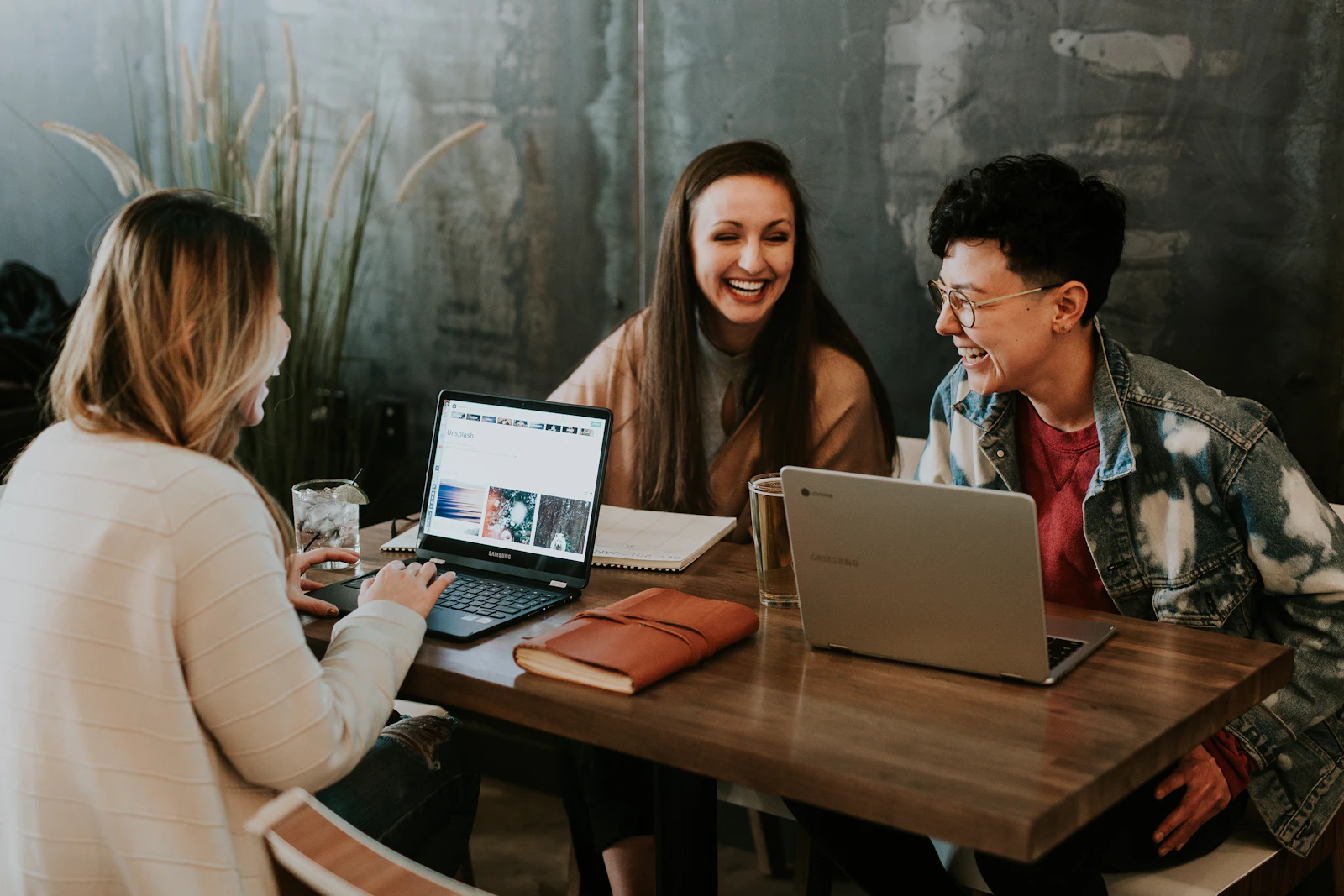 Three colleagues laughing together at a table with a laptop